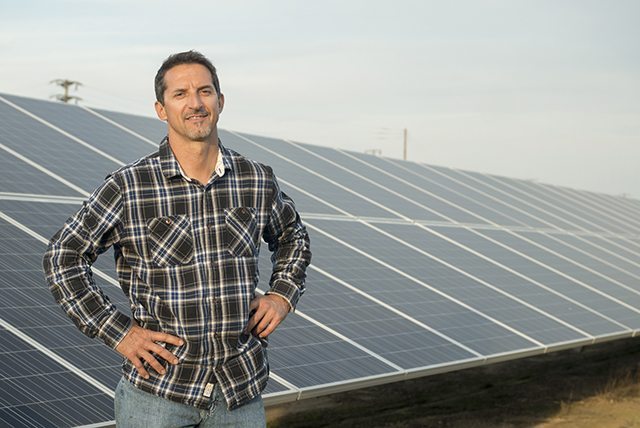 A man standing in front of a row of solar panels in a commercial solar installation on California agricultural land.