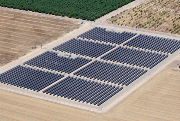 Aerial view of solar panel installation on California agricultural land bordered by almond crop trees and plowed farm land.