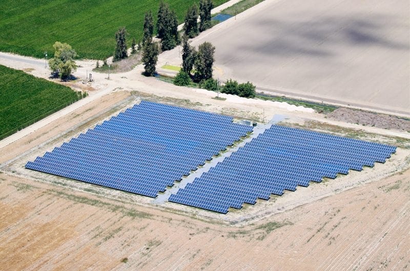 Aerial view of a solar farm installed on California agricultural land and bordered by green crop fields and plowed fields.
