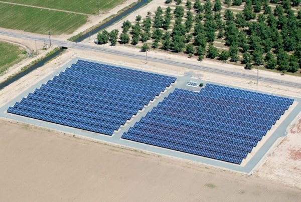 Aerial view of a small solar installation on California agricultural land surrounded on one side by almond crop trees and plowed fields on the other sides.