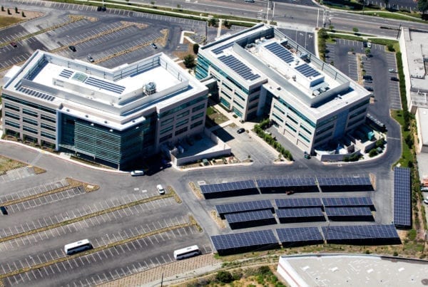Aerial view of two pharmaceutical office buildings with rooftop solar panels and a solar carport in the parking lot.