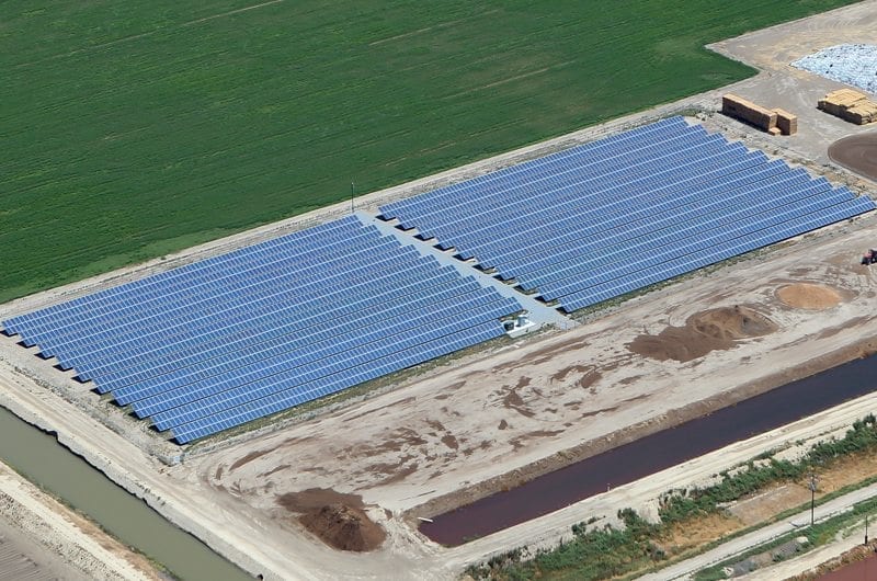 Aerial view of a solar installation on agricultural land in California surrounded by a green field and plowed fields.