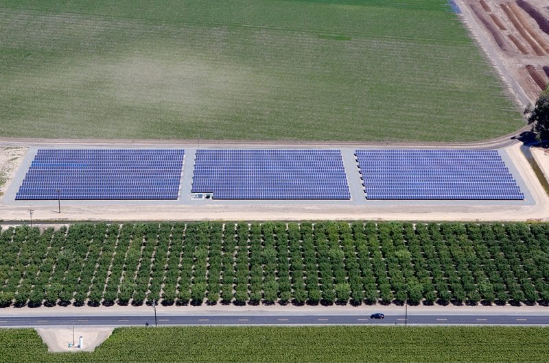 Aerial view of a solar installation on agricultural land in California surrounded by rows of almond crop trees and other crop fields.