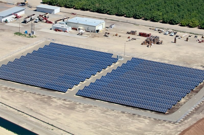 Aerial view of a small solar installation on an almond farm in California and surrounded by commercial agricultural buildings and almond crop trees.