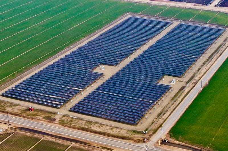 Aerial view of large ground-mounted solar array on California agricultural land surrounded by green pasture land.