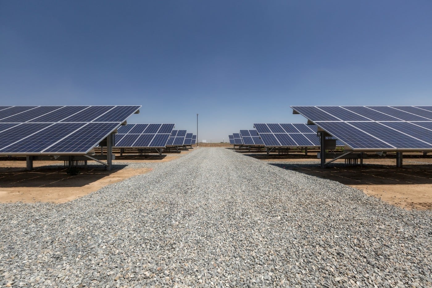 Gravel path between two long rows of ground-mounted solar panels and blue sky at the Joe Simoes dairy farm in Tipton, California.
