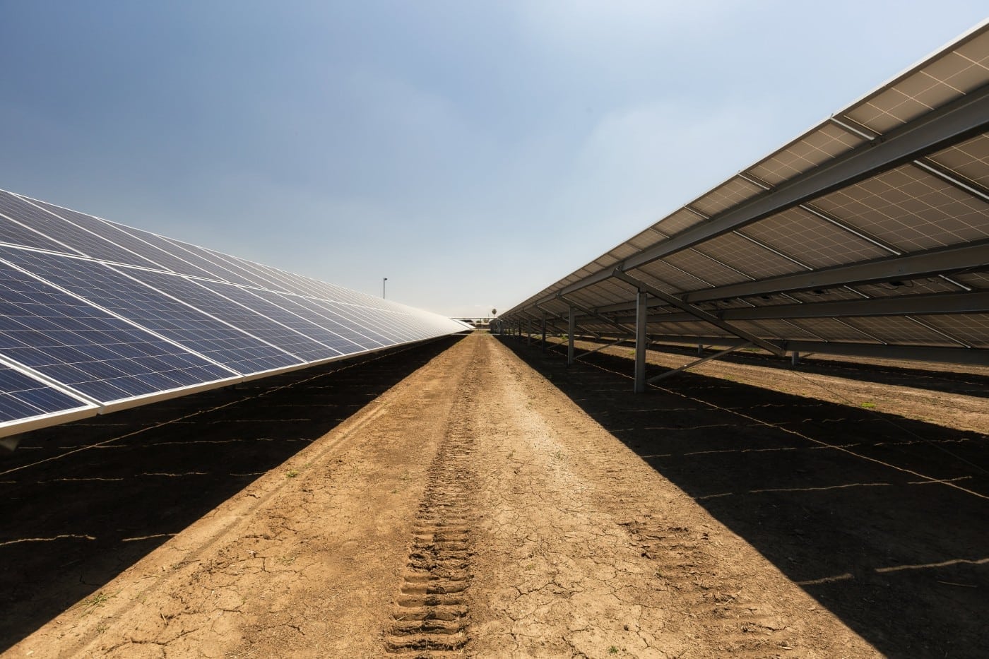 Dirt path between two long rows of ground-mounted solar panels and blue sky at the Joe Simoes dairy farm in Tipton, California.