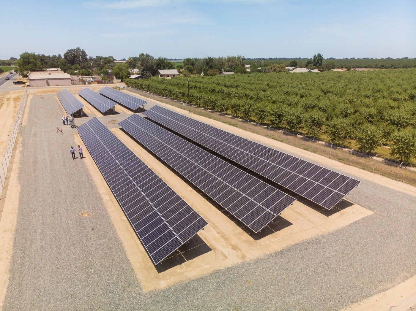 Aerial view of ground-mounted solar panels at Hanse Farms in Hanford surrounded by almond tree crops and farm buildings.