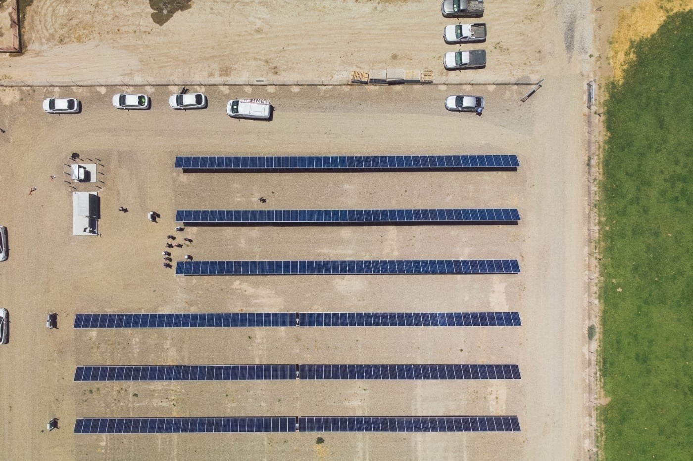 Aerial view of 6 rows of solar panels and parked cars and trucks at the Pedretti Ranch solar installation in El Nido, California.