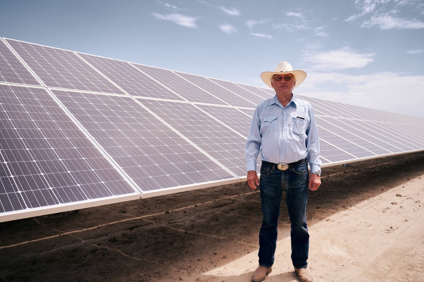 Farmer standing in front of a long row of solar panels constructed at Hanse Farms in Hanford, California.