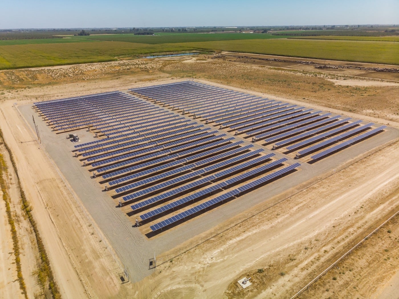 Aerial of large solar panel installation at a dairy farm surrounded by green crop fields in Chowchilla, California.