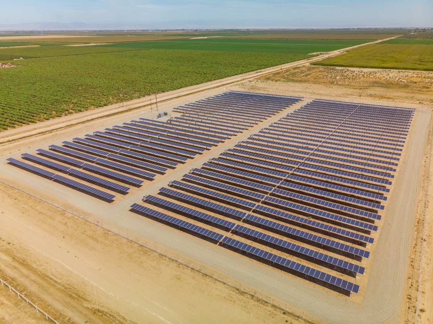 Aerial of large solar panel installation at a dairy farm surrounded by green crop lands in Chowchilla, California.