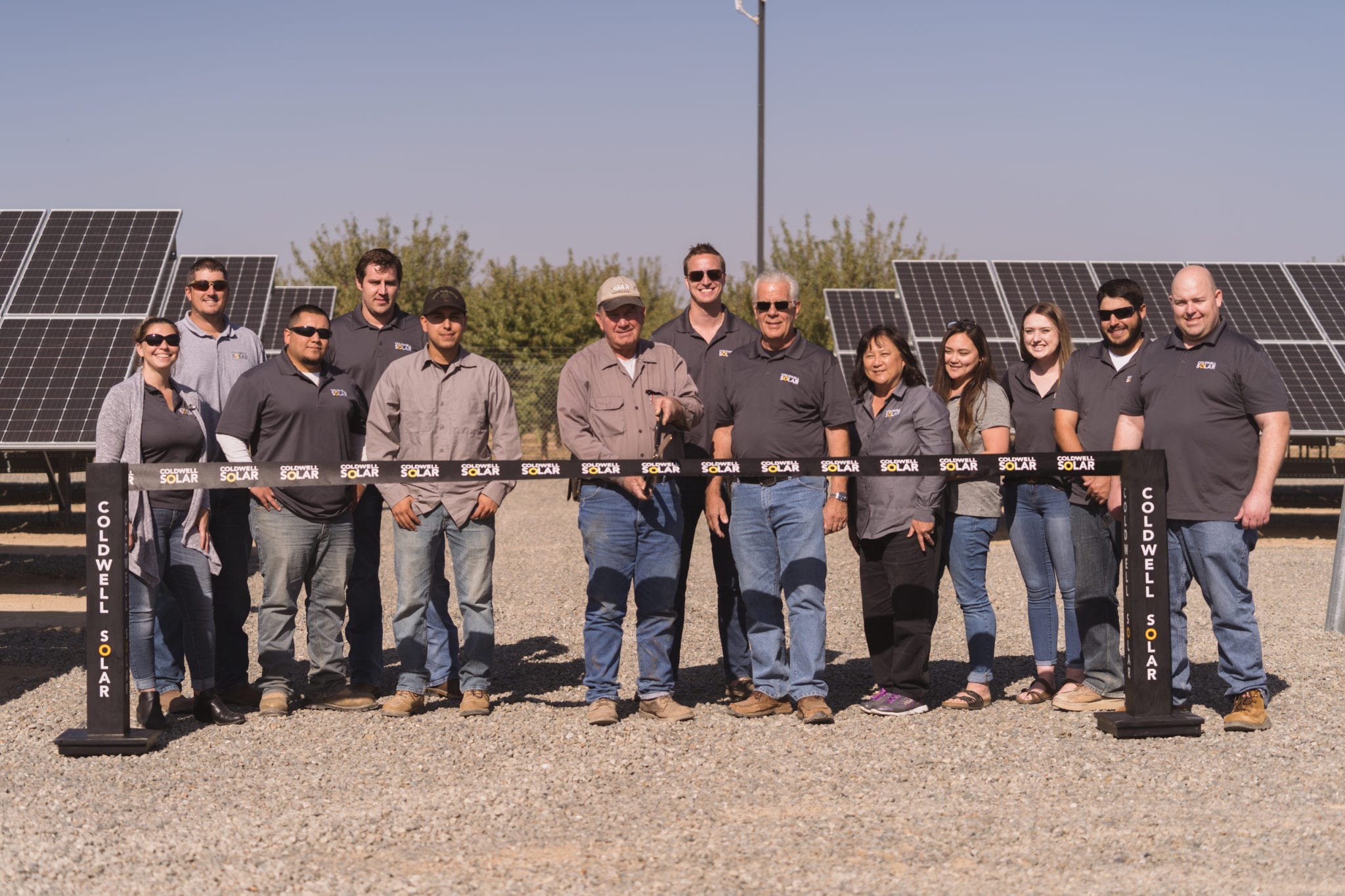 A group of employees from the Dan Habib Ranch in Fresno, California, standing at a ribbon cutting ceremony in front of rows of newly constructed solar panels.