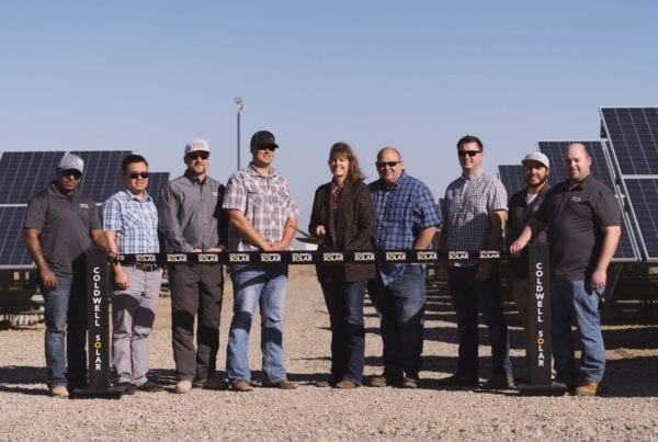 A group of employees from the Hammonds Ranch in Firebaugh, California, standing at a ribbon cutting ceremony in front of rows of newly constructed solar panels.