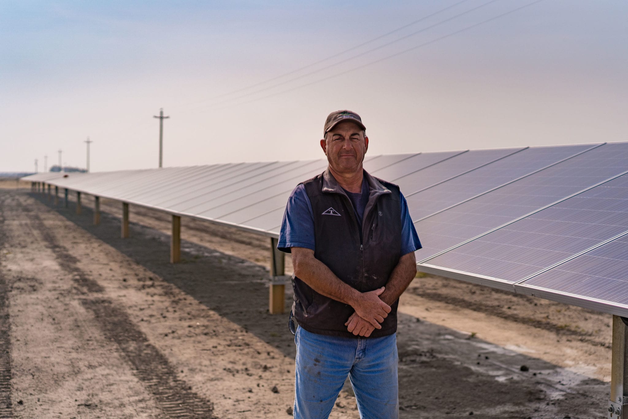 Man standing in front of a long row of ground-mounted solar panels at a farm in Madera, California.