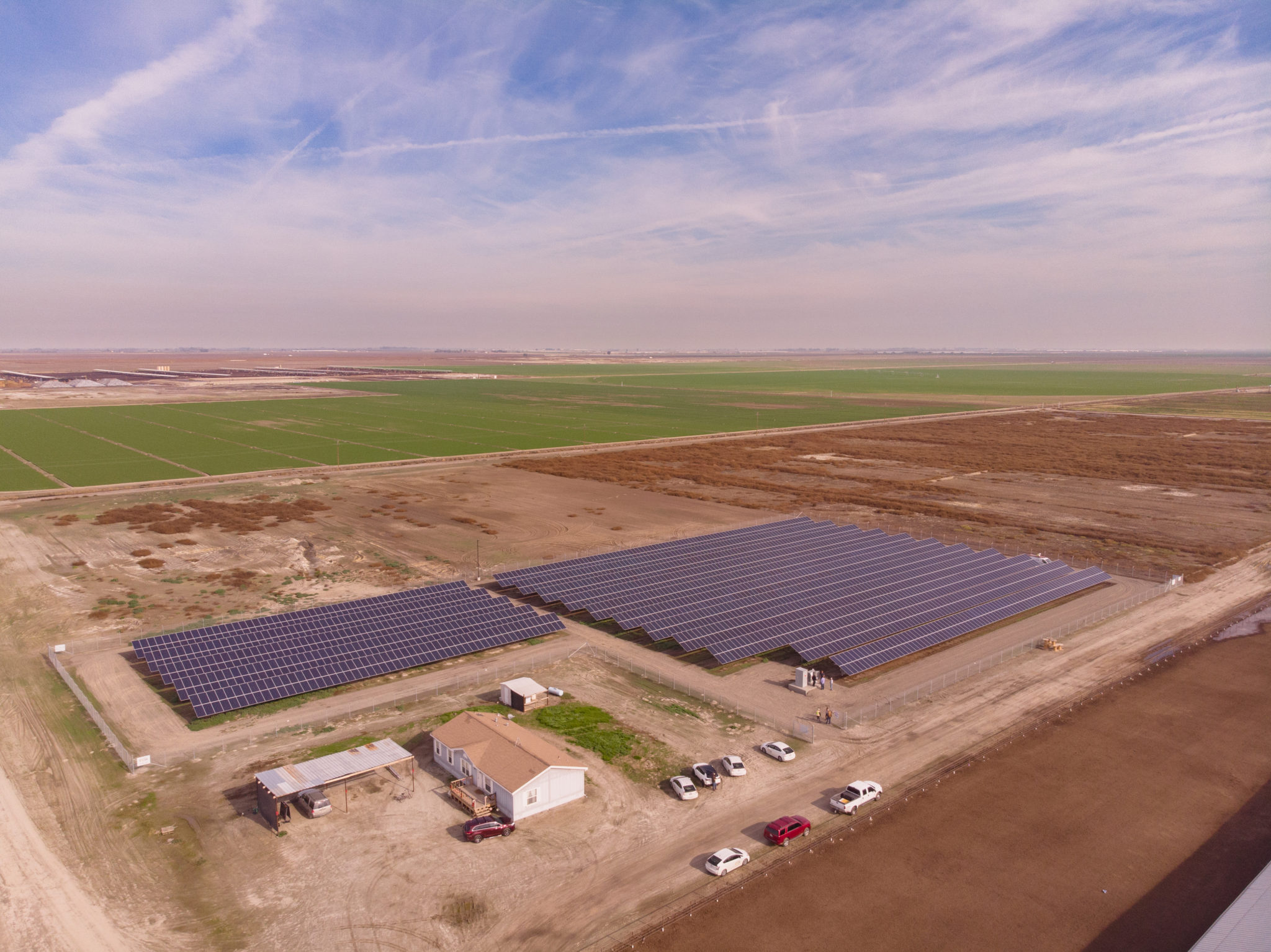 Aerial view of the solar installation surrounded by brown farmland and a farm building at Lakeshore Dairy in Hanford, California.