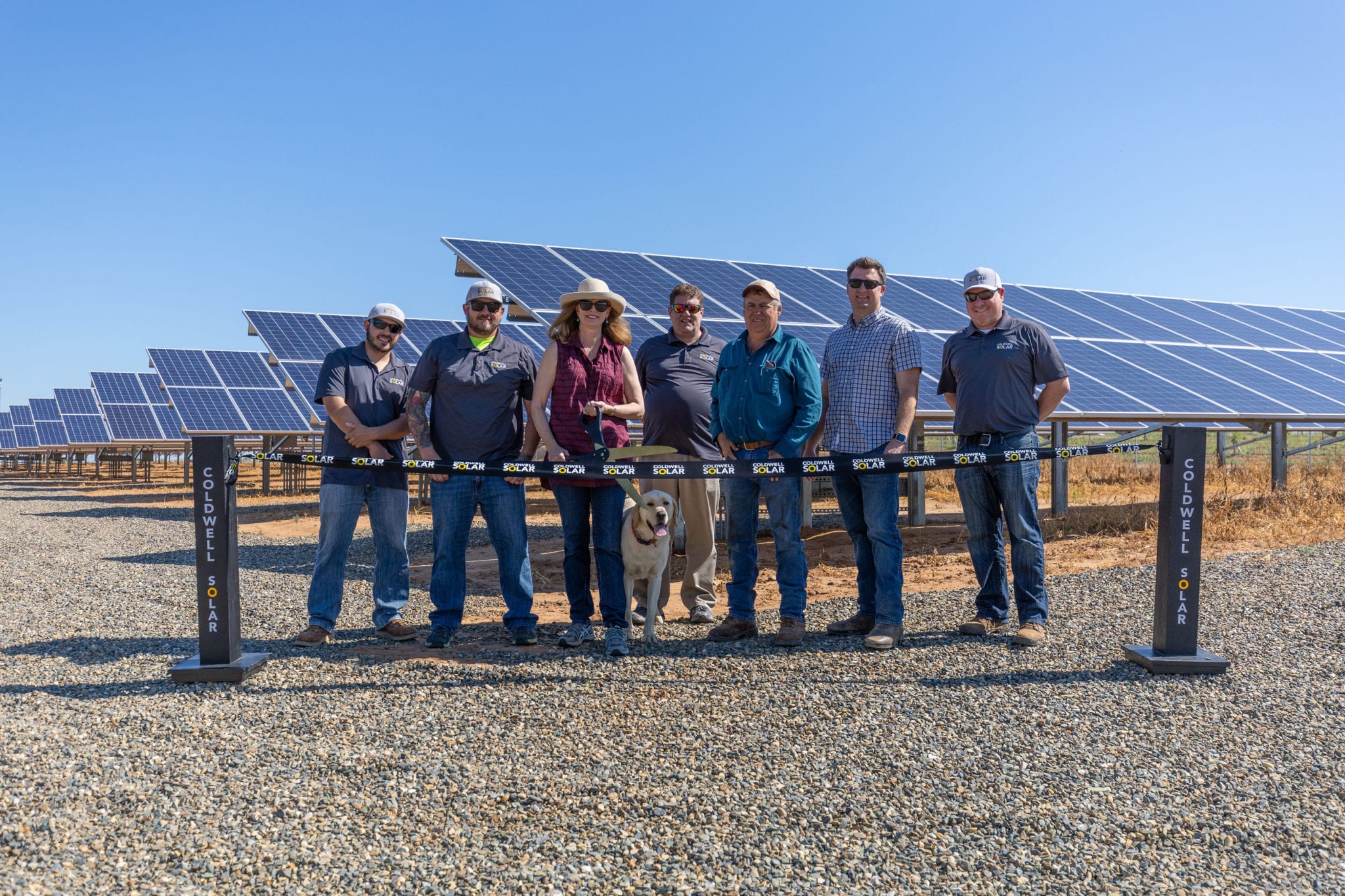 People standing at a ribbon cutting in front of a solar installation at an almond orchard in Winton, California.