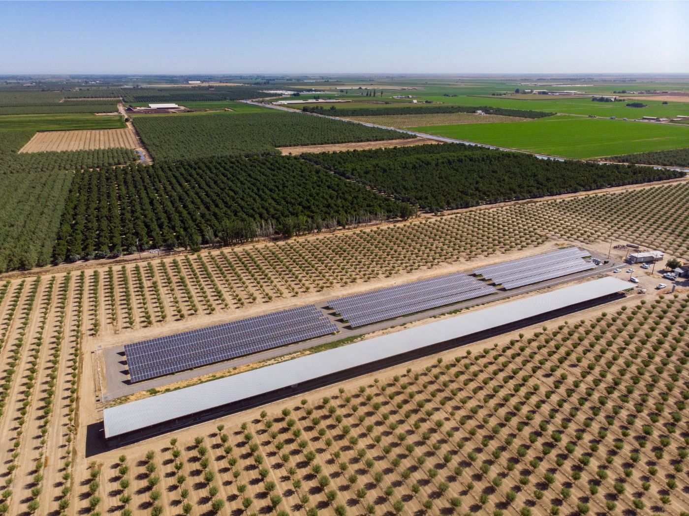 Aerial view of solar farm at Iyer Farms surrounded by planted crops and trees and green farmland in the background.