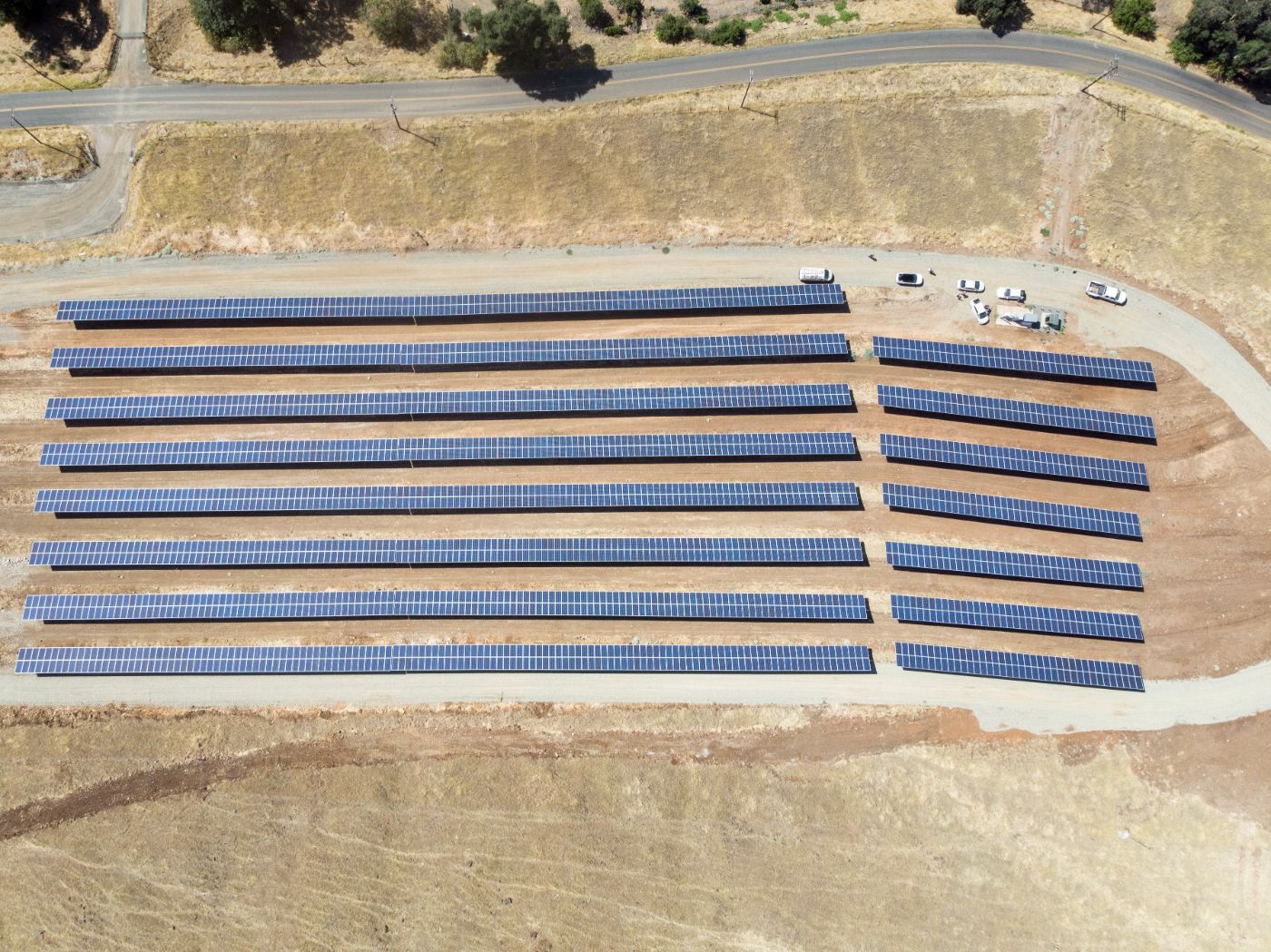 Aerial view of a small solar farm on brown grassland next to a two-lane road.