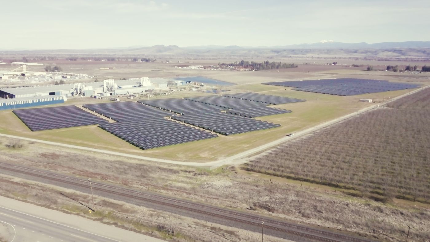 Aerial view of the completed Sierra Pacific Industries solar farm at Red Bluff, California with crops in the foreground and mountains in the background.