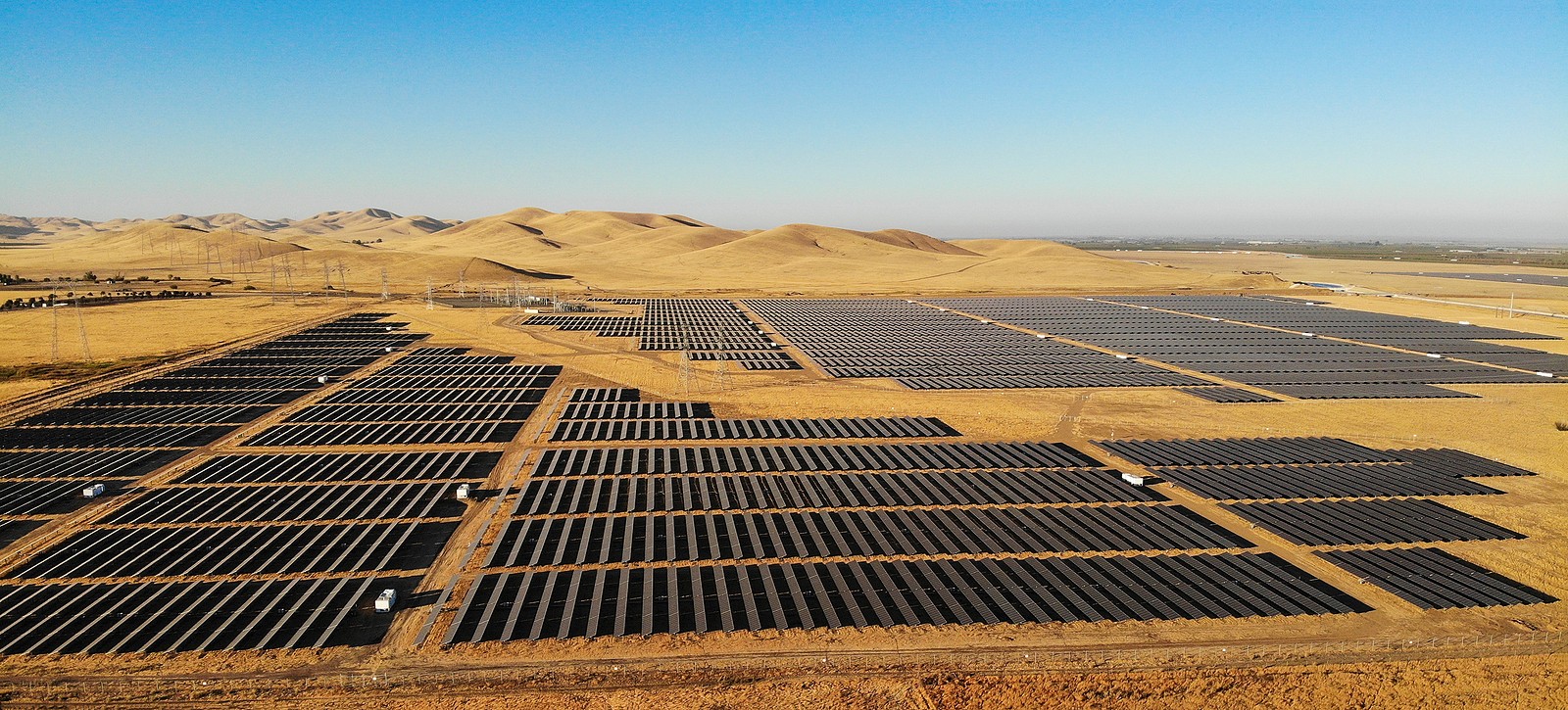 Large utility-scale solar farm in California desert with sand hills in the background.