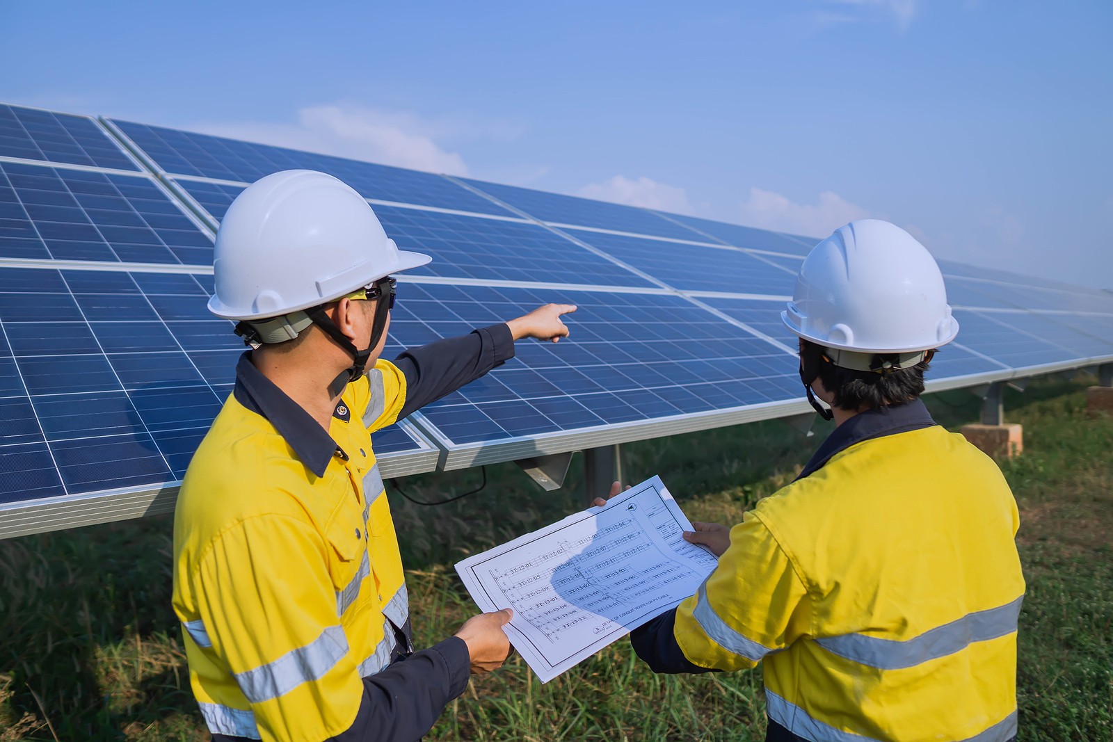 Two solar engineerings studying a blue print and pointing at the ground-mounted solar panels.