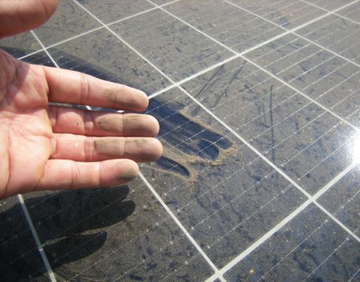 Close up view of a dusty solar panel and a man's hand with dirty fingers and dust marks left on the panel.
