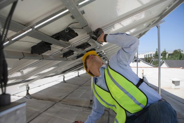 Solar company engineer underneath a roof-mounted commercial solar panel inspecting it.
