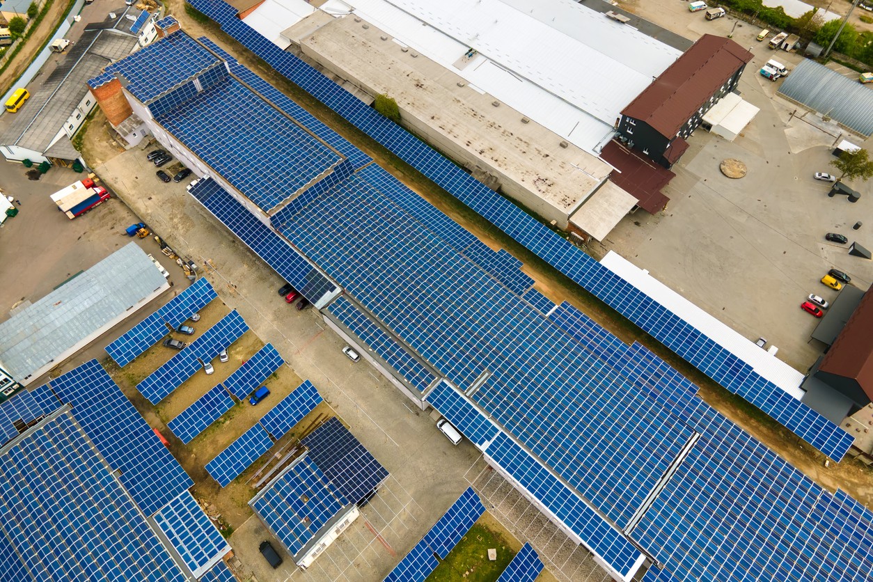 Aerial view of a long warehouse with blue roof-mounted solar panels and carports.
