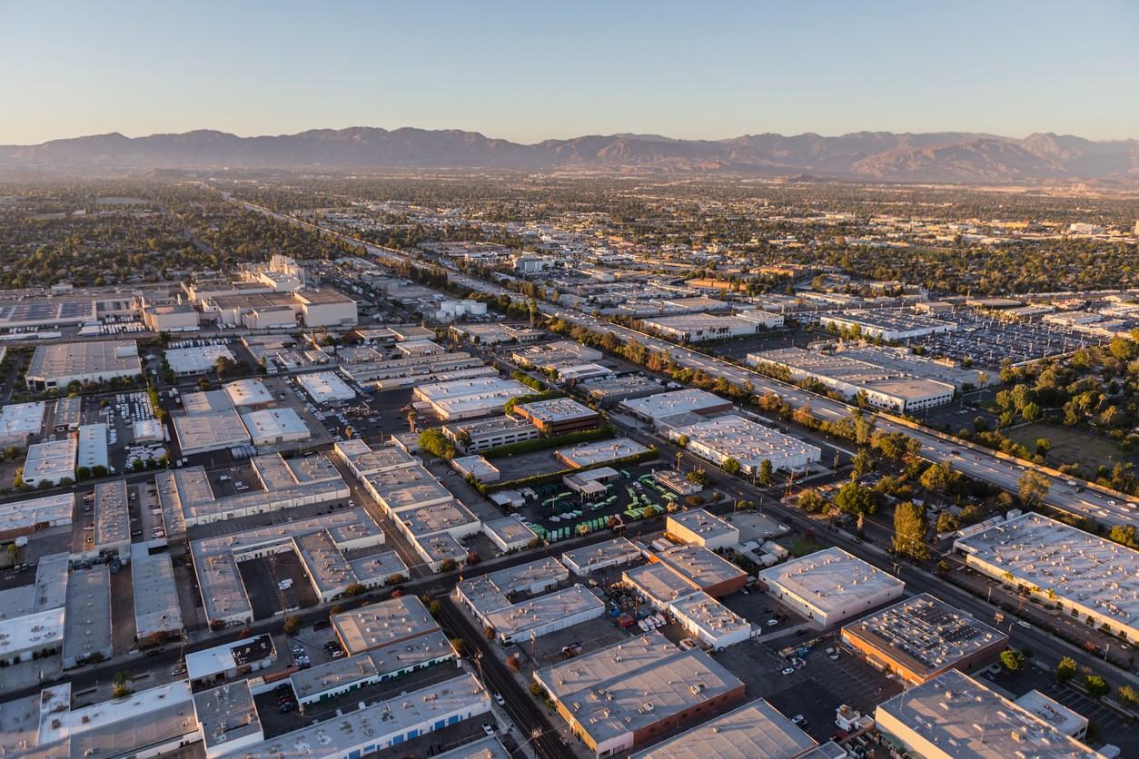 Aerial view of dozens of California warehouses with mountains and blue sky in the background.