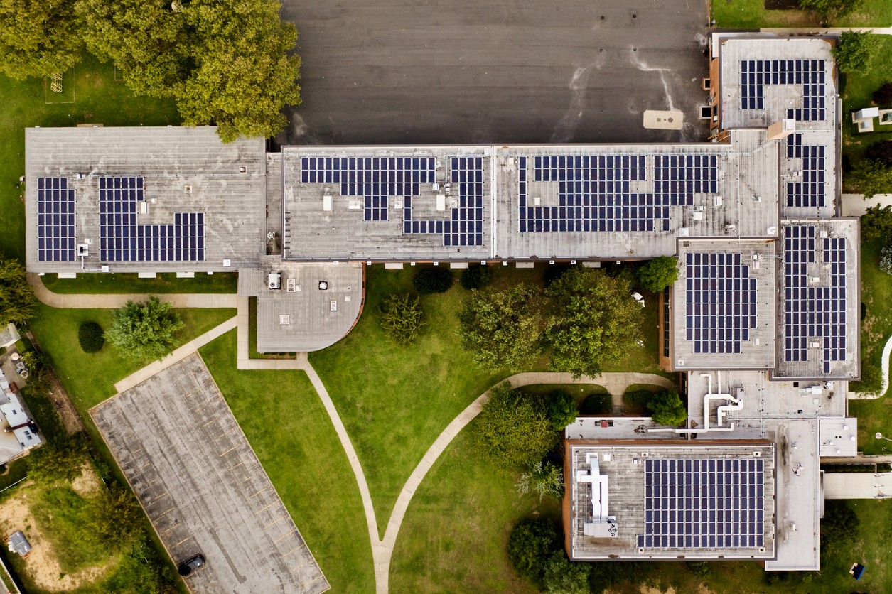 Aerial view of an L-shaped school building with solar panels mounted on the roof and surround by green landscaping.