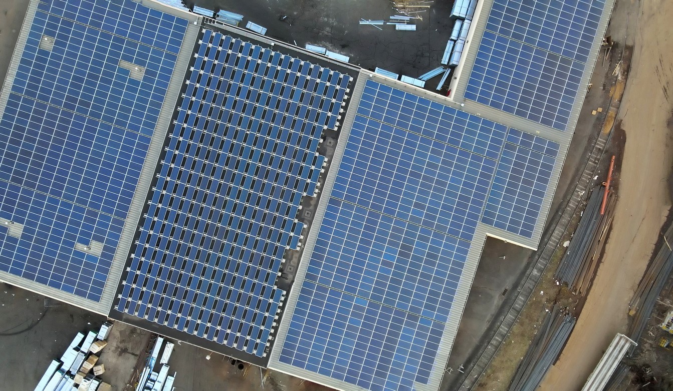 Aerial view of solars panels on the roofs of an L-shaped warehouse building.