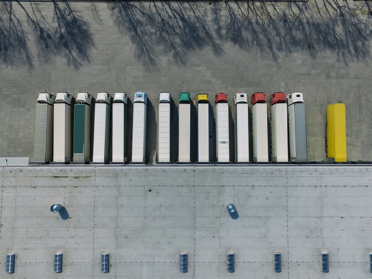 Aerial view of a row of semi trucks parked at warehouse loading docks.