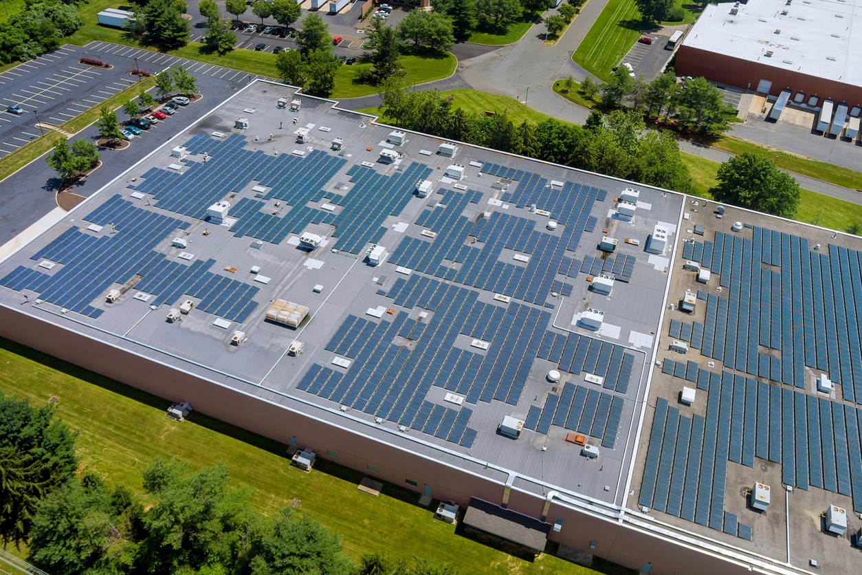Aerial view of solar installation on a California warehouse roof surrounded by green trees and landscaping.