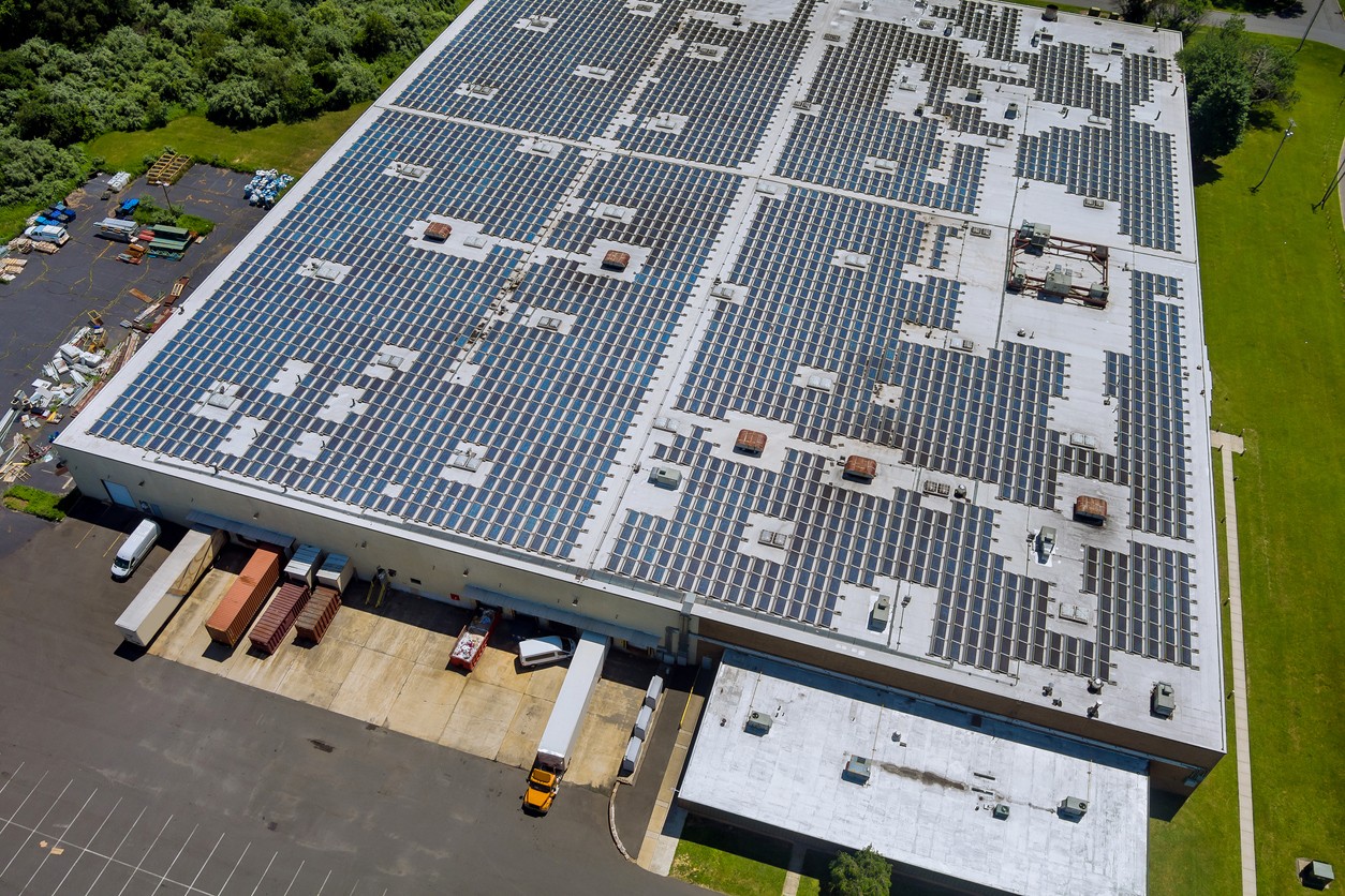 Aerial view of solar panels dotting the roof of a warehouse with trucks parked at loading docks and green landscaping.
