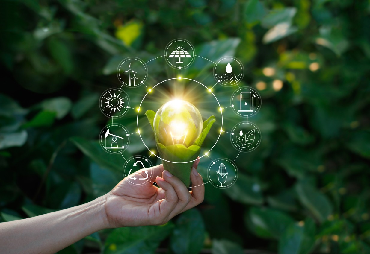 A photographic concept of solar energy with a woman's hand holding a green plant growing a light bulb with green energy-related icons connected to it.