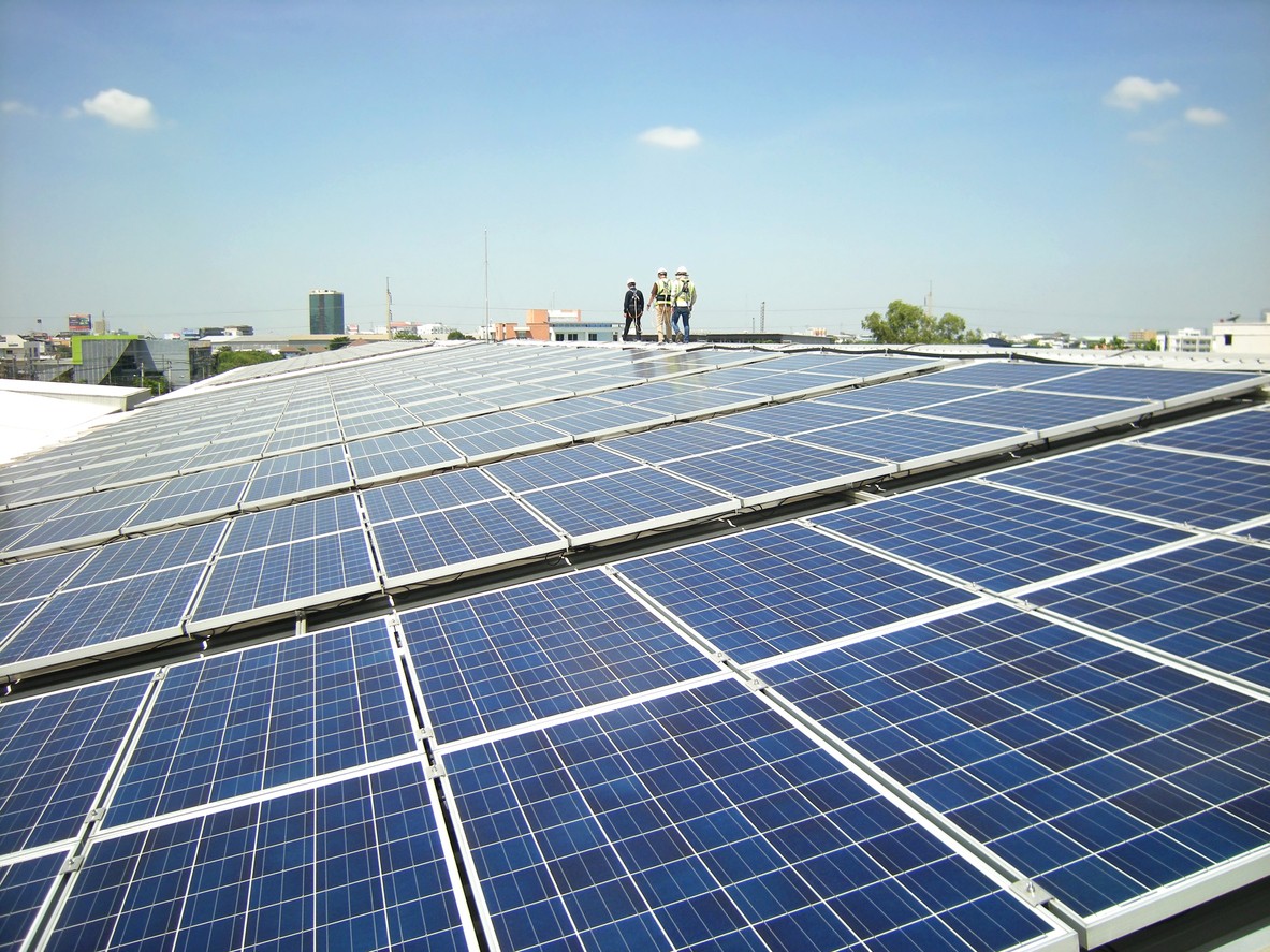 Three solar company workers walking on the roof of a commercial building with solar panels in the foreground.