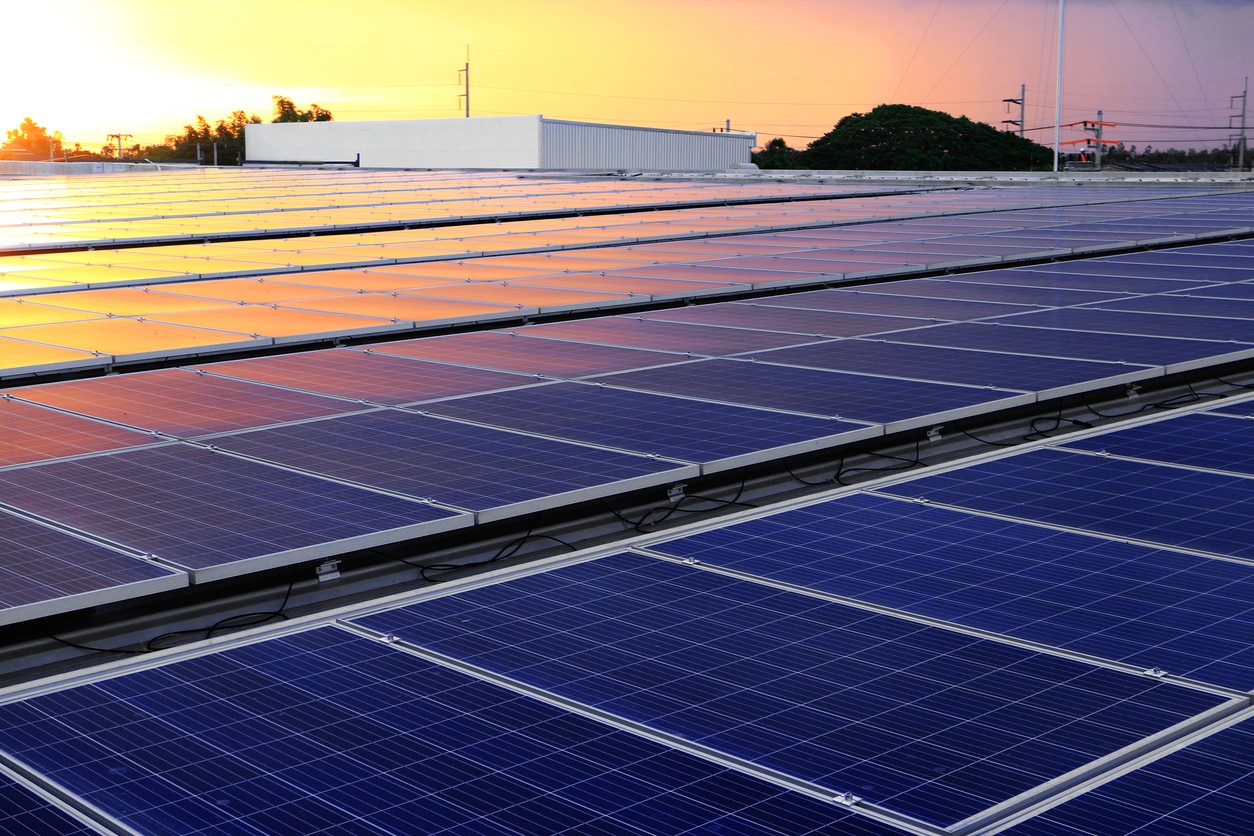 Looking across rows of solar panels on a commercial building roof at sunset.