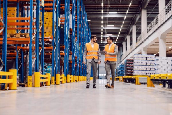 Two warehouse operators walking through an aisle of a warehouse. 