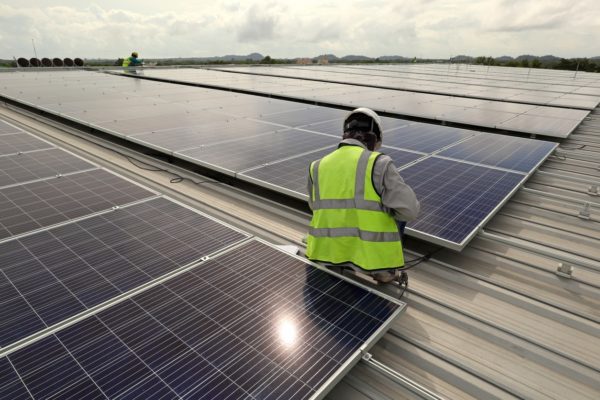 Two solar company workers on the roof of a commercial building working on solar panels.