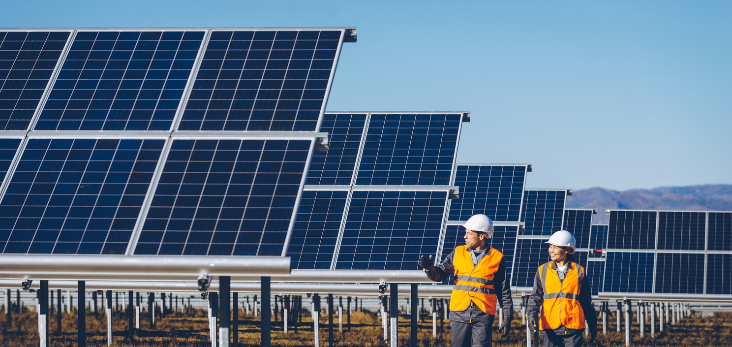 Two solar company workers walking and talking among rows of large blue solar panels on a solar farm.