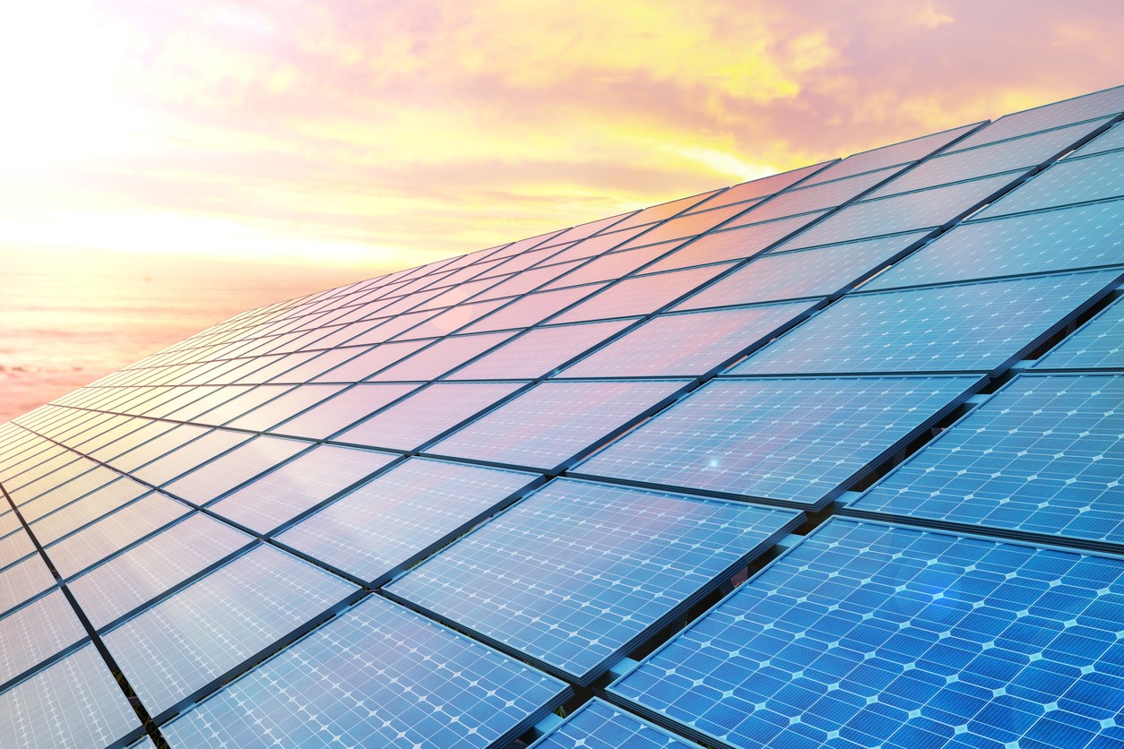 Looking across a row of blue solar panels at sunrise.