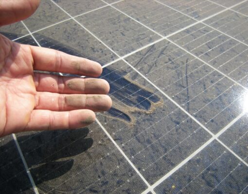 Close up view of man's hand showing dust on a solar panel.