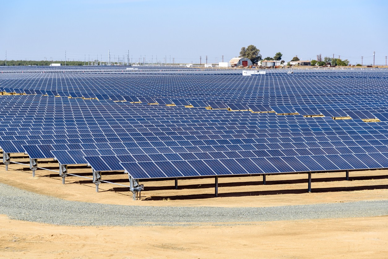 Rows of blue solar panels in a large solar farm adjacent to a working farm on California agricultural land.