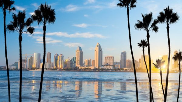 San Diego skyline with blue sky and water in foreground. 