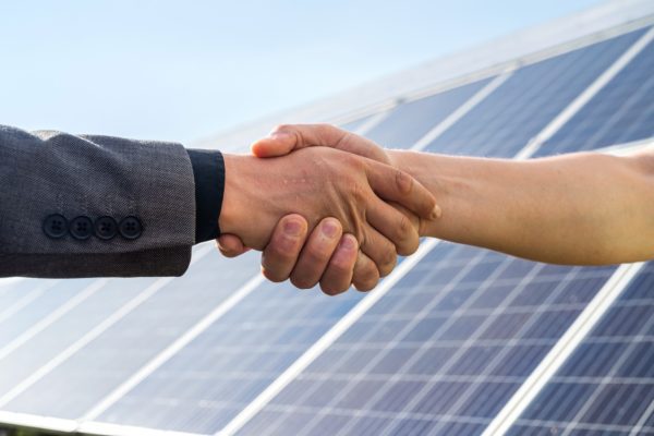 Solar engineer and businessman shaking hands in front of a commercial rooftop solar installation.