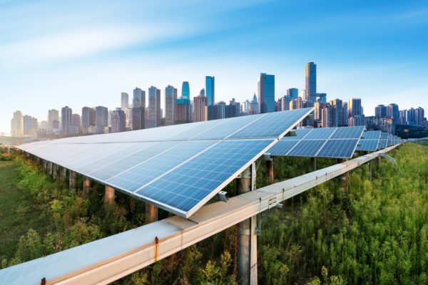 Ground-mounted solar panels set among trees against a blue sky and downtown city skyline.