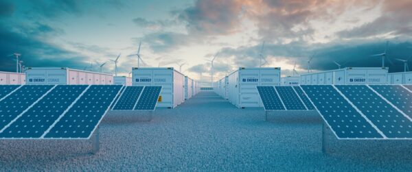 Solar battery storage units with solar panels in the foreground and wind turbines in the background. 