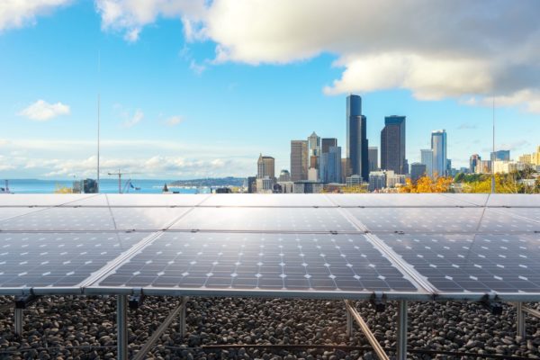 Ground-mounted solar panels in foreground against a downtown city skyline and bay in the background.