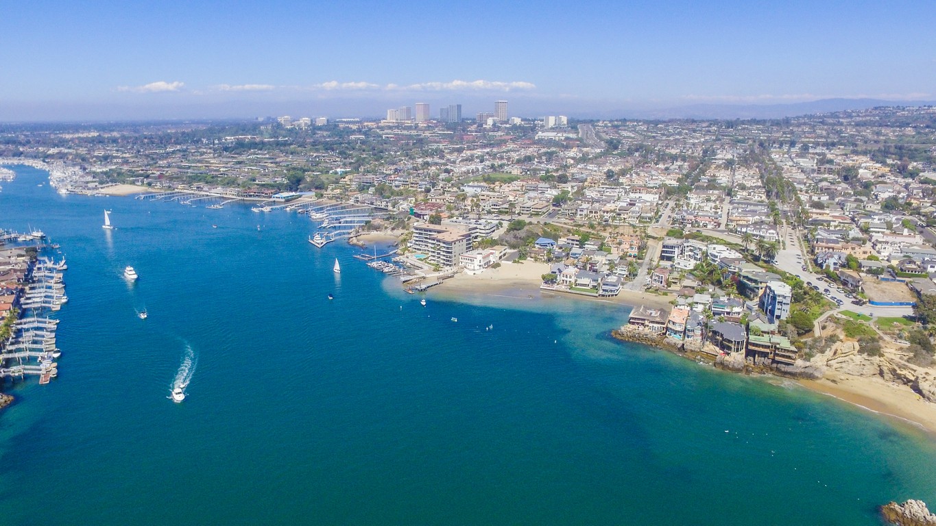 Aerial view of the Orange County California coast with boats on the water and a downtown skyline in the background.